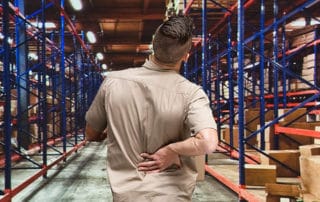 Man in a warehouse holding his back in pain, representing workplace injuries and workers' compensation