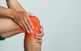 Close-up of a man touching his painful knee highlighted in red, showing symptoms of joint pain or inflammation or anterior cruciate ligament (ACL) tear.