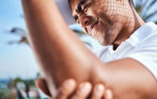 young man standing alone and suffering from a tennis elbow injury during a game of tennis.