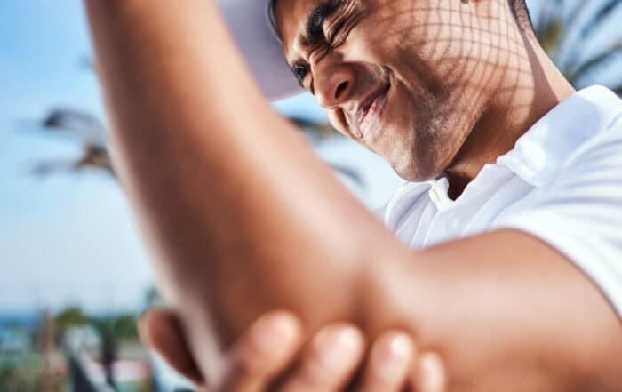 young man standing alone and suffering from a tennis elbow injury during a game of tennis.