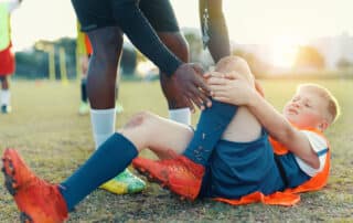 A teenager lying on the football field in pain, clutching his leg after a sports injury.
