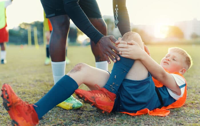 A teenager lying on the football field in pain, clutching his leg after a sports injury.