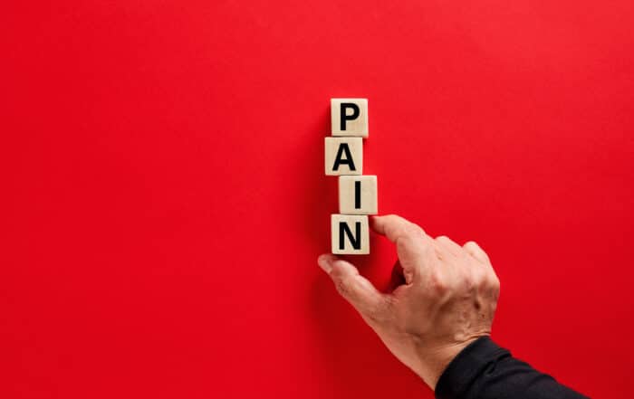 Male hand arranging the wooden blocks with the word pain on red background with copy space.