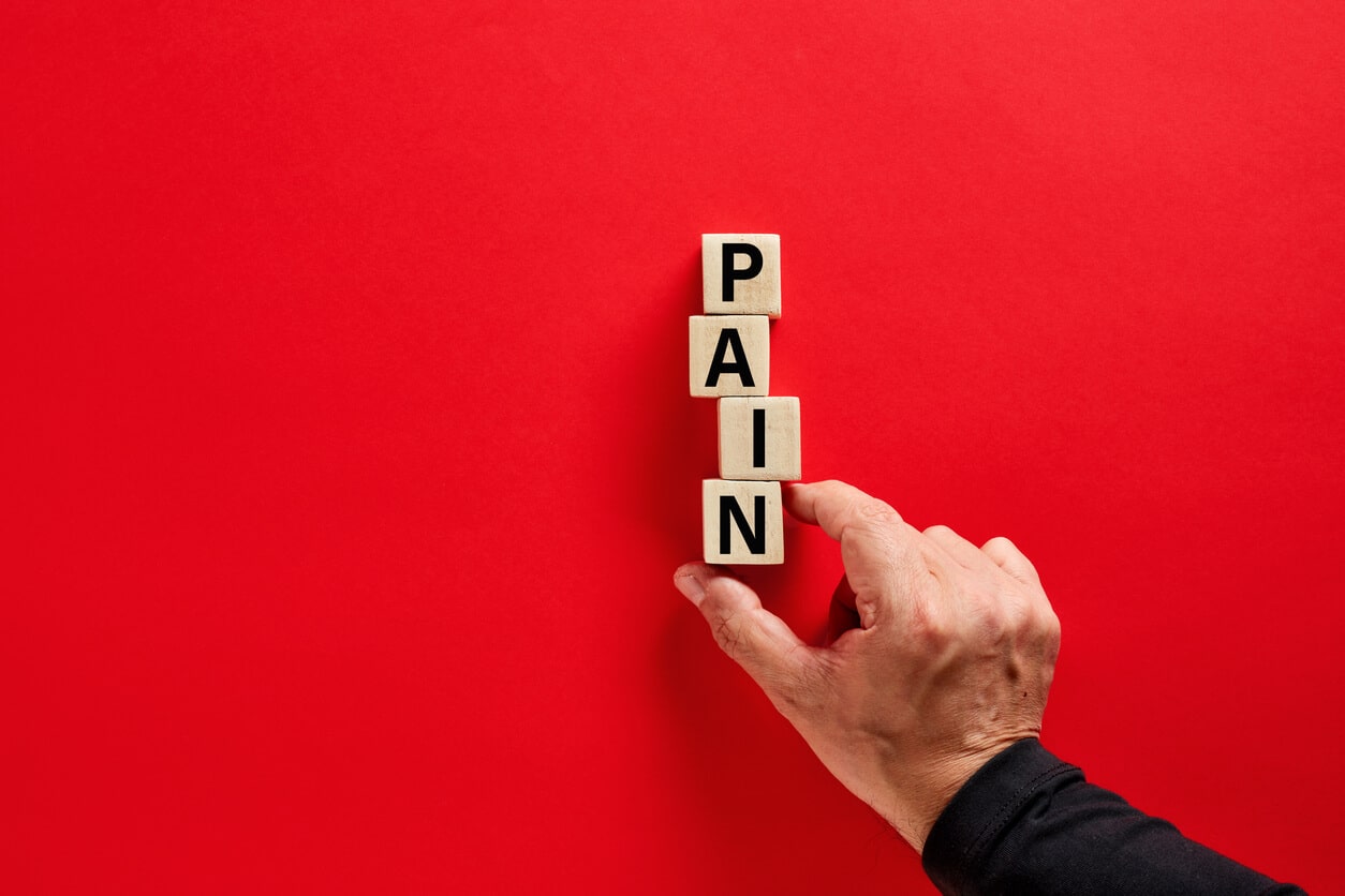 Male hand arranging the wooden blocks with the word pain on red background with copy space.