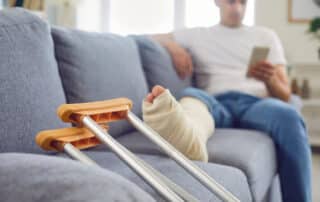 Close-Up Of Man Broken Leg And Crutches Resting On Sofa.