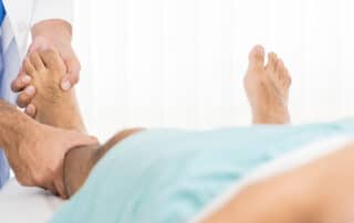 Doctor examining and treating patient with fractured and broken leg while on the bed in hospital.
