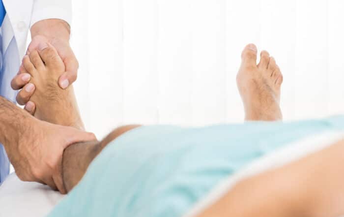 Doctor examining and treating patient with fractured and broken leg while on the bed in hospital.