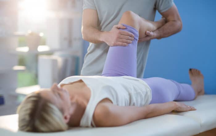 Male physiotherapist giving knee massage to female patient during sports orthopedic urgent care.