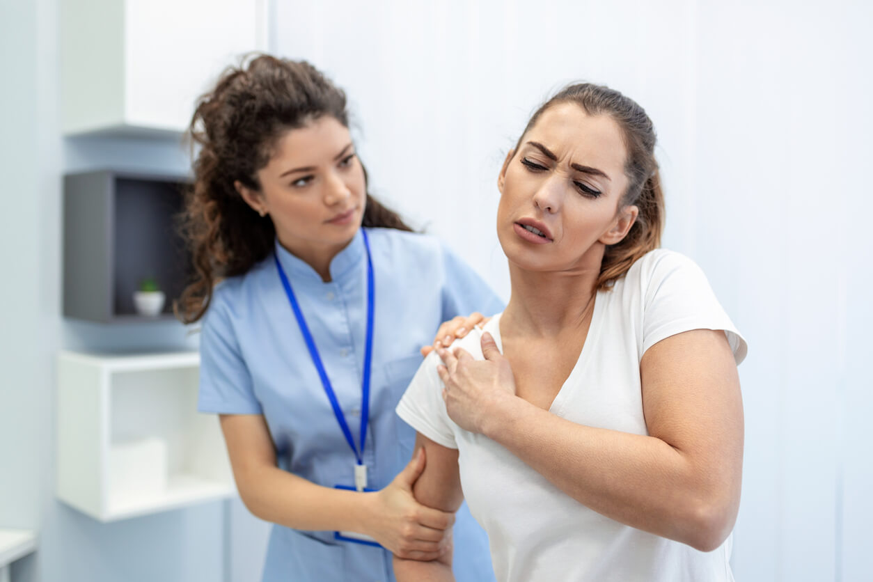 A woman in medical uniform fixing woman patients shoulder and back joints in manual therapy clinic during visit.
